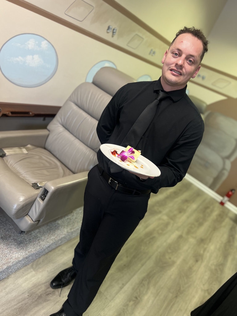 Student in a black uniform presenting a plated course in the mock cabin